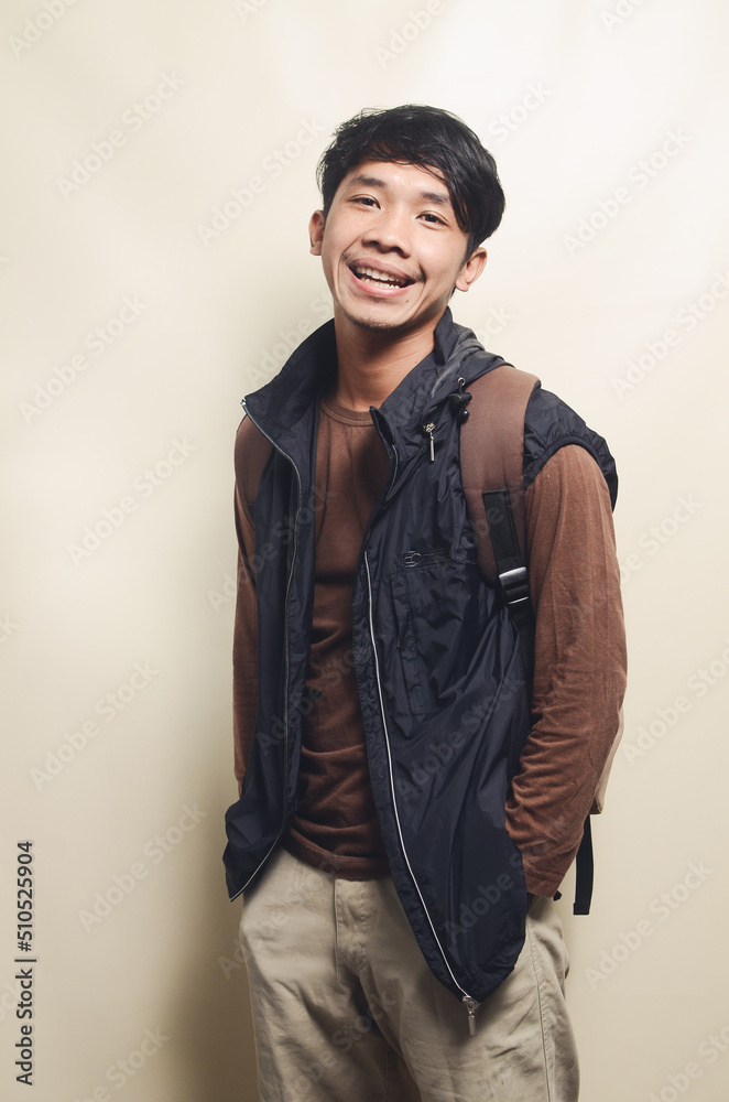 Portrait of Asian young man leaving for college wearing brown t-shirt and black vest isolated on background Portrait of Asian young man leaving for college wearing brown t-shirt and black vest isolated on background