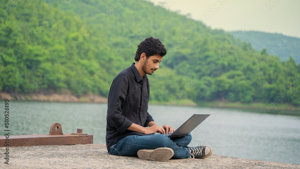Young man working on a laptop and sitting in the nature, Workation and Digital Nomad concept.