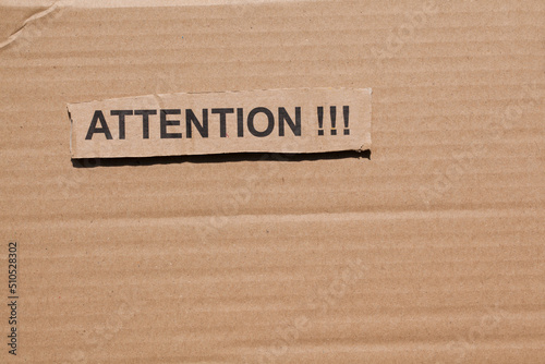 Cut out piece of cardboard with the words "ATTENTION!!!" written on it. Brown cardboard in the background.