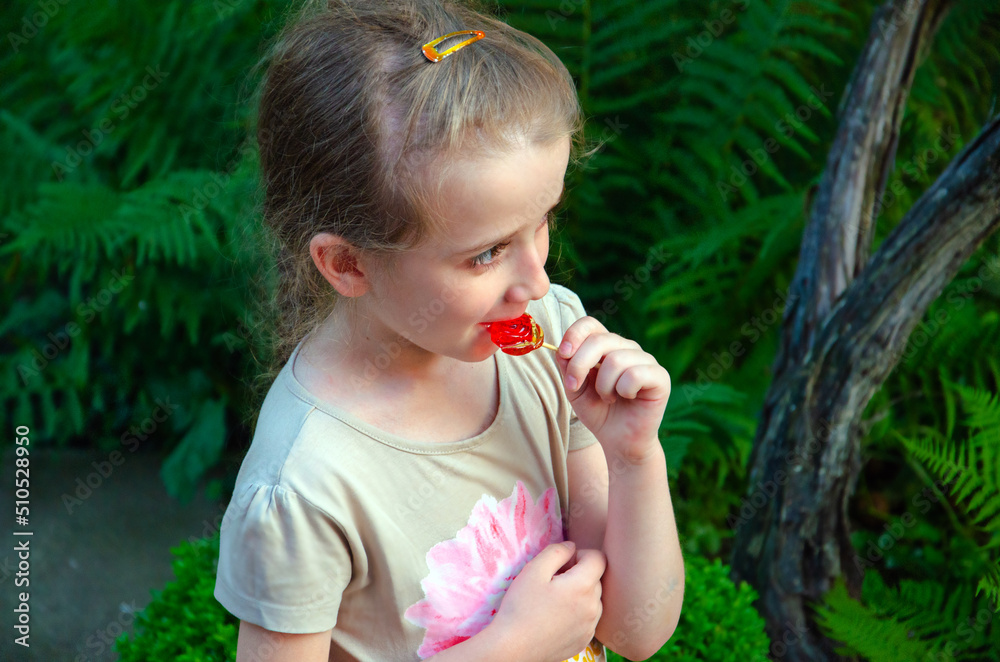 little girl eats a lollipop, child eats a red lollipop while walking in the yard little girl eats a lollipop, child eats a red lollipop while walking in the yard