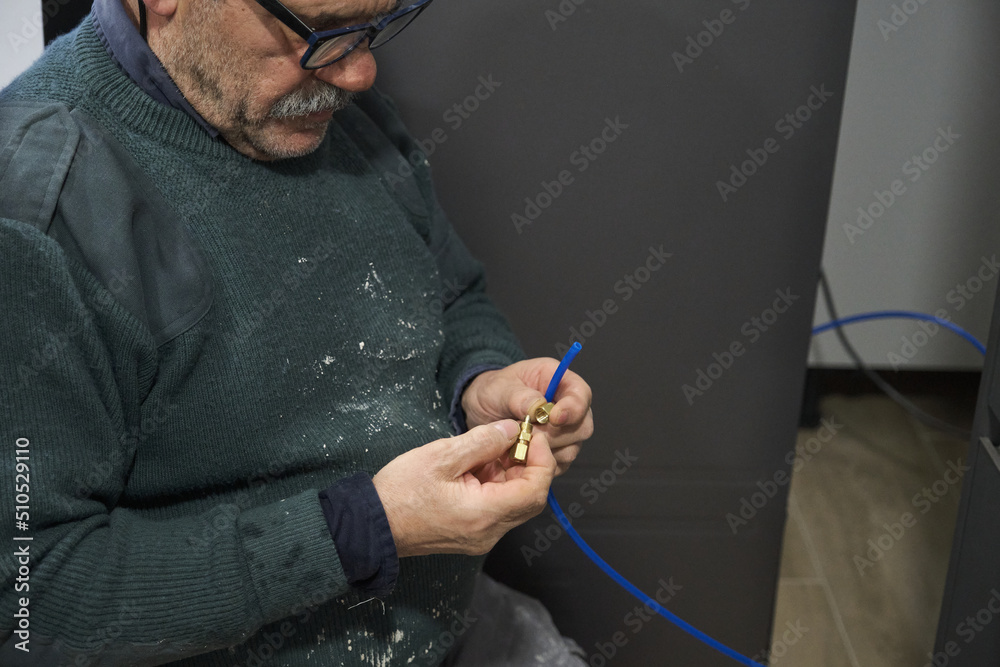 Mature technician installing water filter to an american refrigerator in kitchen. - obrazy, fototapety, plakaty 