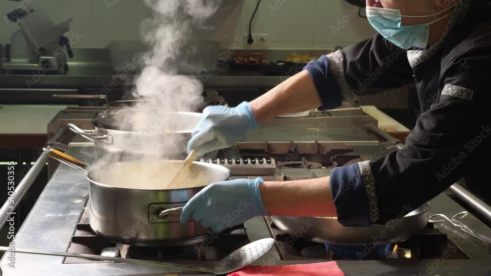 Cook wearing mask and gloves moves the food in professional kitchen in Spain Cook wearing mask and gloves moves the food in professional kitchen in Spain