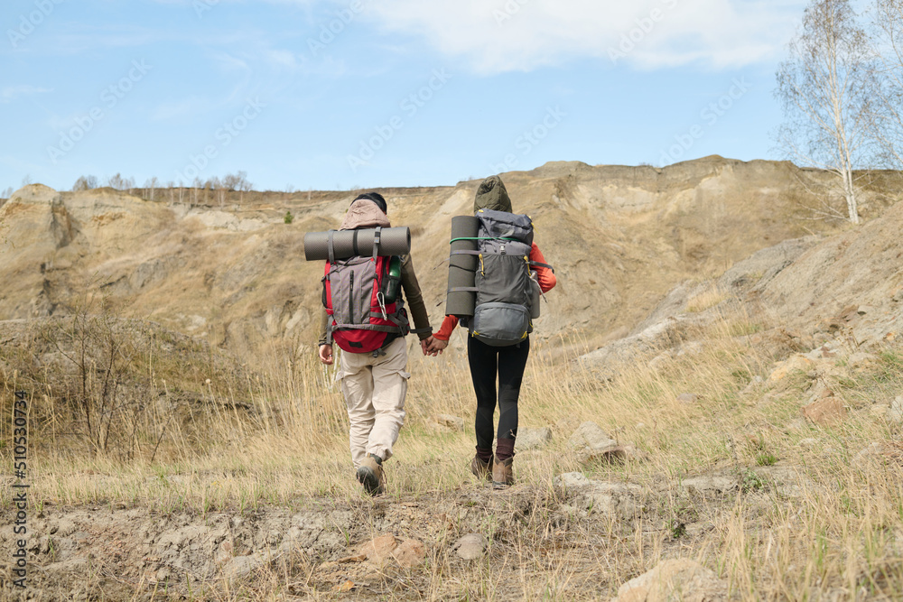 Horizontal back view long shot of two unrecognizable female friends hiking together on spring day somewhere around quarry