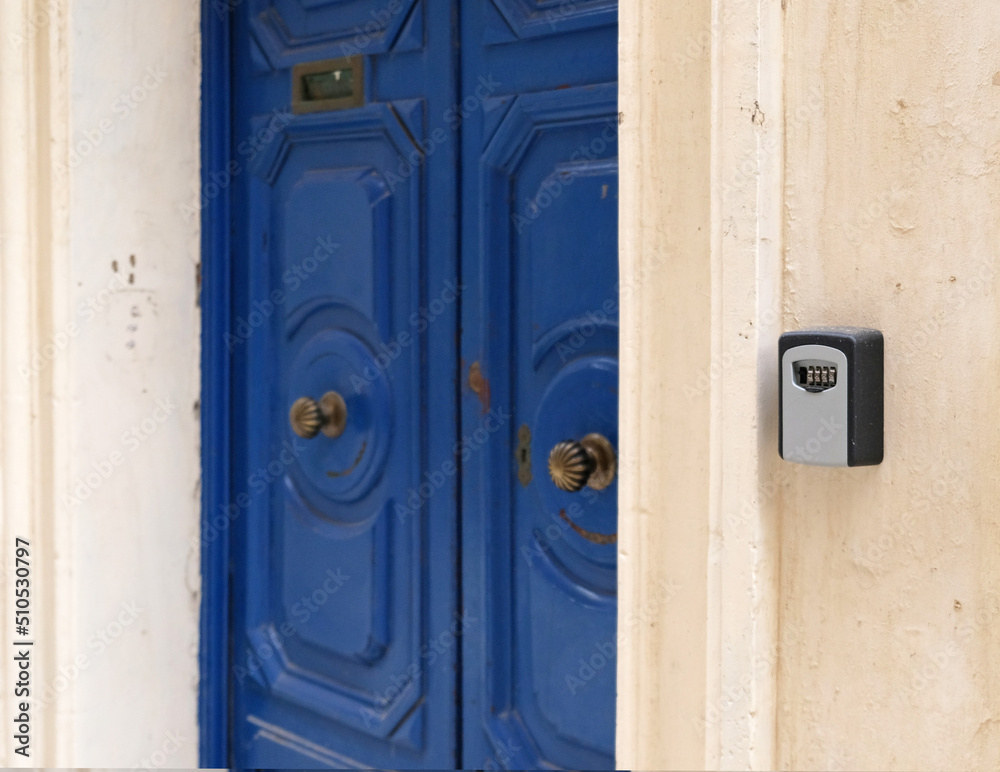 Smart key lock mounted on wall for renting apartment. Safe Key Box is used when the guest arrives at the touristic flat and the host can't open the door. Safe access to living space. Blue vintage door