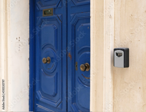 Smart key lock mounted on wall for renting apartment. Safe Key Box is used when the guest arrives at the touristic flat and the host can't open the door. Safe access to living space. Blue vintage door