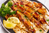 grilled chicken kebabs sprinkled with chopped fresh parsley over flatbreads on plate on white wooden table, close-up