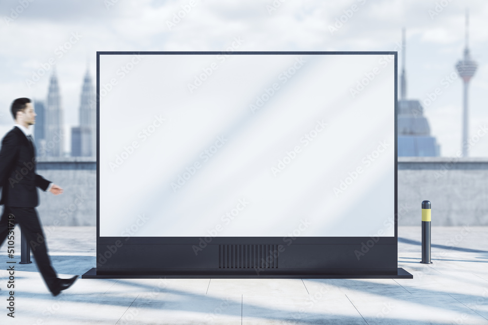 Businessman walking past empty white rectangular poster on light city background. Mock up. Retail and commercial concept. Businessman walking past empty white rectangular poster on light city background. Mock up. Retail and commercial concept.
