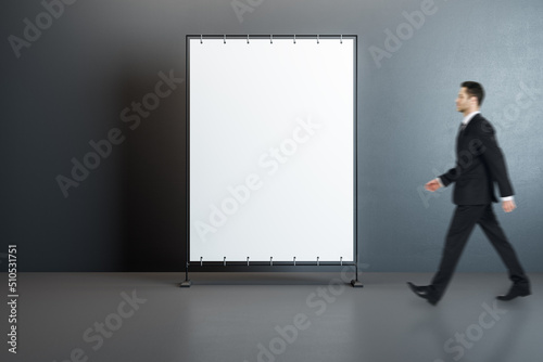 Front view on blank white poster with place for your text or logo and walking man in black suit on grey wall background, mock up © Who is Danny