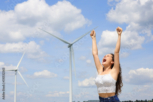 Excited woman raising arms celebrating in a wind farm