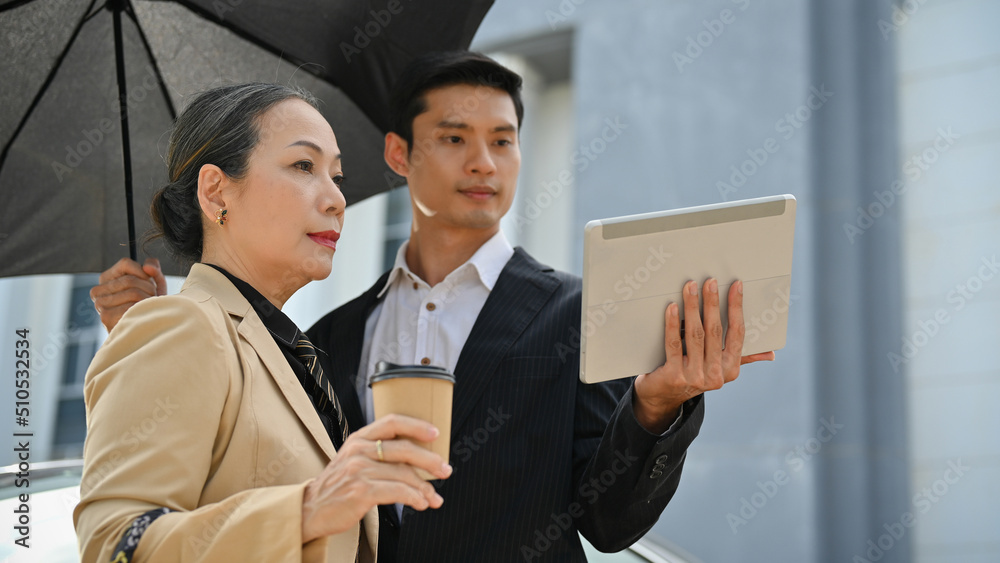 Asian aged businesswoman with male assistant, checking her building at the construction site.