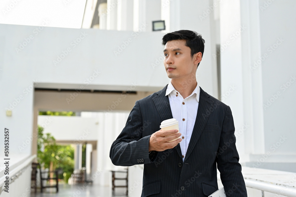Fototapeta premium Handsome asian male boss standing outside of the building with a coffee cup in his hand.