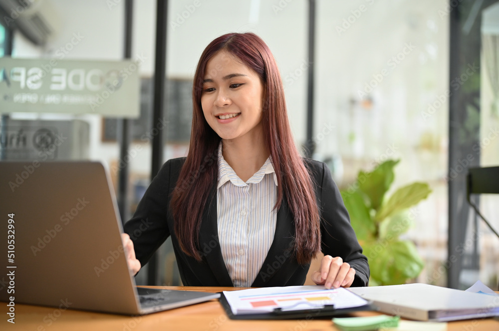 Attractive young asian businesswoman working on her financial paperwork and using laptop. Attractive young asian businesswoman working on her financial paperwork and using laptop.