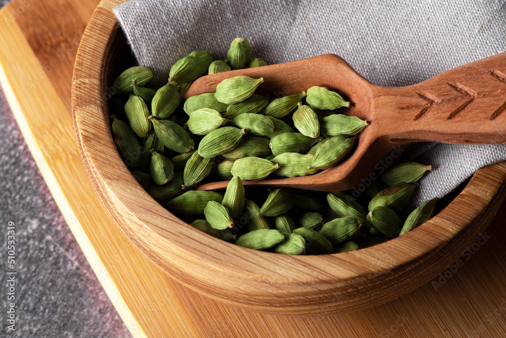 Green cardamom in wooden bowl and spoon. Dry cardamom spice. Cardamom seeds macro shot. Green cardamom in wooden bowl and spoon. Dry cardamom spice. Cardamom seeds macro shot.