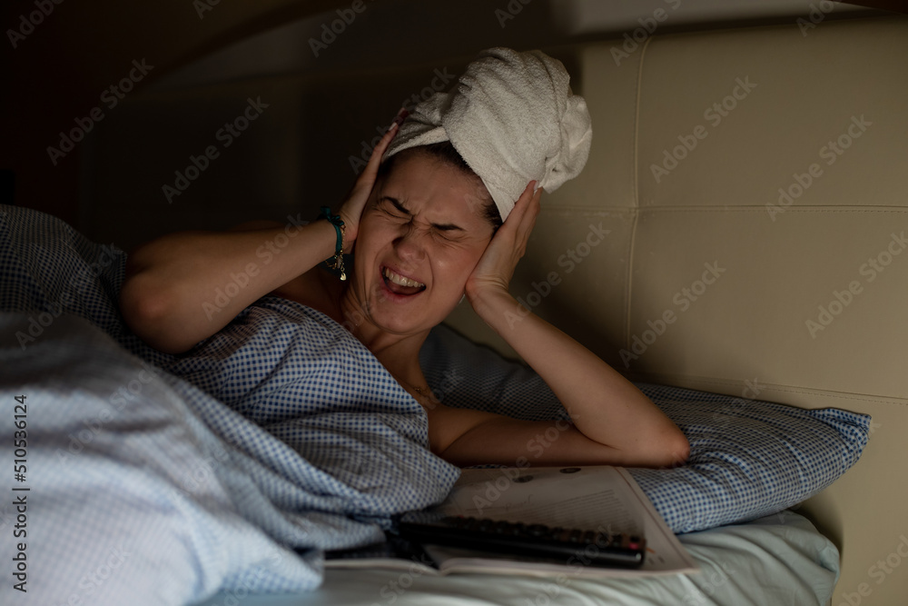 Young woman with white towel wrapped around head lying on bed suffering from headache, earache covering ears with hands. Young woman with white towel wrapped around head lying on bed suffering from headache, earache covering ears with hands.