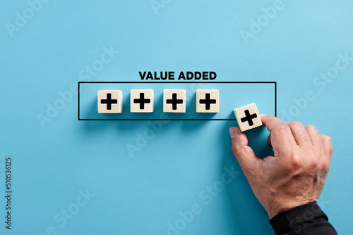 Male hand puts the wooden cube with plus icon with the word value added. Profit, benefit growth and development in business