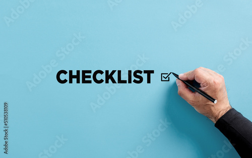 Male hand puts checkmark next to the word checklist. Checklist, to do list, prioritize or reminder for project plan.