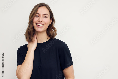 Portrait of young smiling woman looking happy on white background. Big smile on her face, looking beautiful and cute with hands touching her neck.