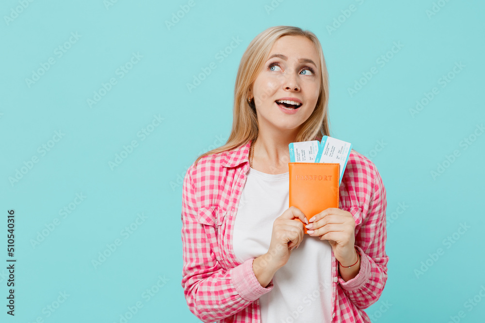 Traveler tourist pensive fun woman in pink shirt hold passport boarding tickets isolated on plain pastel light blue background. Passenger travel abroad on weekends getaway. Air flight journey concept. Traveler tourist pensive fun woman in pink shirt hold passport boarding tickets isolated on plain pastel light blue background. Passenger travel abroad on weekends getaway. Air flight journey concept.