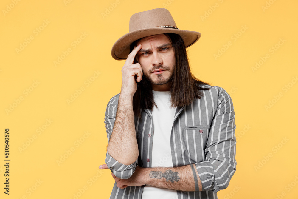 Young disappointed unhappy man he 20s wears striped grey shirt white t-shirt hat look camera prop up head forehead isolated on plain yellow color background studio portrait. People lifestyle concept. Young disappointed unhappy man he 20s wears striped grey shirt white t-shirt hat look camera prop up head forehead isolated on plain yellow color background studio portrait. People lifestyle concept.