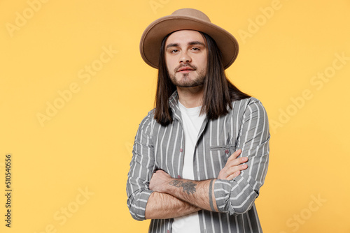Young confident cool fun man he 20s wears striped grey shirt white t-shirt hat look camera hold hands crossed folded isolated on plain yellow color background studio portrait People lifestyle concept