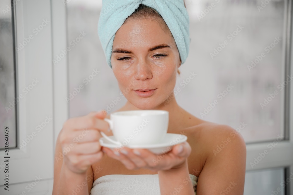 Young serene relaxed woman in spa bath towel drinking hot beverage tea coffee after taking shower bath at home. Beauty treatment, hydration concept. Young serene relaxed woman in spa bath towel drinking hot beverage tea coffee after taking shower bath at home. Beauty treatment, hydration concept.