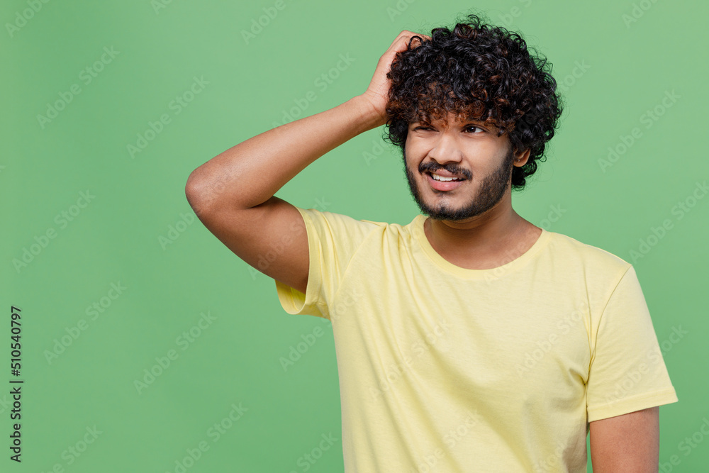 Young sad mistaken confused puzzled Indian man 20s wearing basic yellow t-shirt scratch hold head look aside isolated on plain pastel light green background studio portrait. People lifestyle concept. Young sad mistaken confused puzzled Indian man 20s wearing basic yellow t-shirt scratch hold head look aside isolated on plain pastel light green background studio portrait. People lifestyle concept.