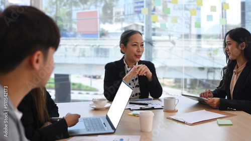 Smiling young female team leader coach discussing market research results to diverse business people at briefing