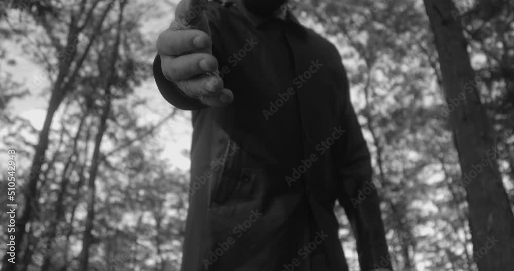 A hand of unrecognizable person in dark clothes throwing the first handful of earth into the grave against cemetery with trees. Tall unrecognizable man on funeral.  Black and white