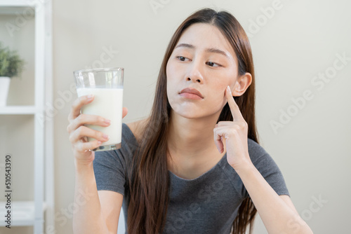 Allergy asian young woman, girl looking, holding glass of milk, face in thinking before drink milk as it may upset her stomach ache, pain. Lactose intolerance and dairy food , health problem concept.