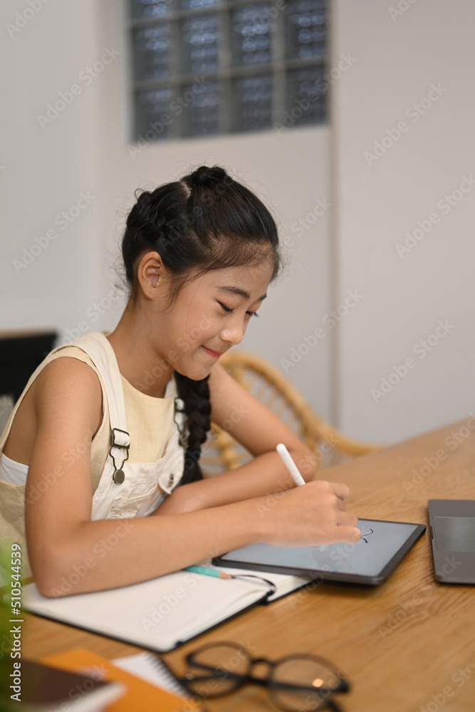 Smiling Asian girl doing homework on digital tablet, studying through online learning system Smiling Asian girl doing homework on digital tablet, studying through online learning system