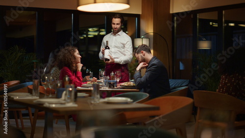 Fotografi Waiter pouring wine bottle to fancy couple table at night restaurant dinner date