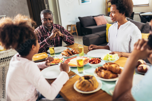 A multi-generational African-American family enjoying food at their dinner table.