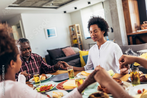 A multi-generational African-American family saying grace at dinner table and holding hands