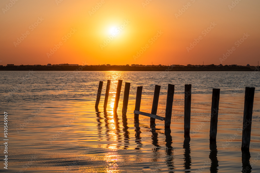 Obraz premium Beautiful red and orange sunset over the sea. The sun goes down over the sea. A flock of cormorants sits on a old sea pier in orange sunset light