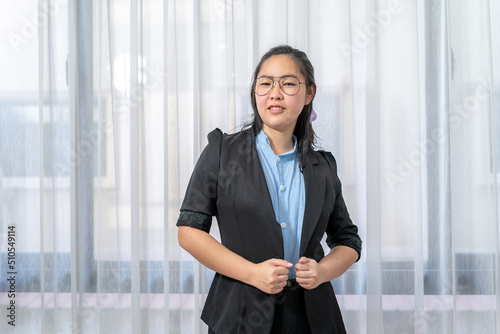 Little entrepreneur Asian eyeglasses woman with confident pose in black suit stands in front of window and curtain. photo