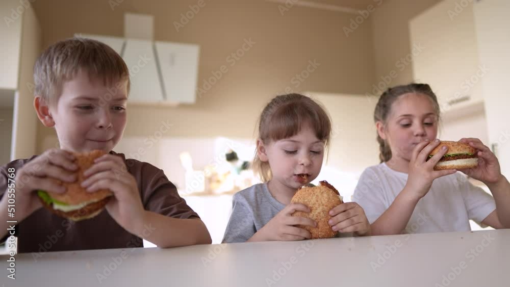 children eat burgers. fast food burger. a group of small children in the kitchen greedily eat fast food burgers. big family small kids having breakfast in the morning in fun the kitchen eating burger children eat burgers. fast food burger. a group of small children in the kitchen greedily eat fast food burgers. big family small kids having breakfast in the morning in fun the kitchen eating burger