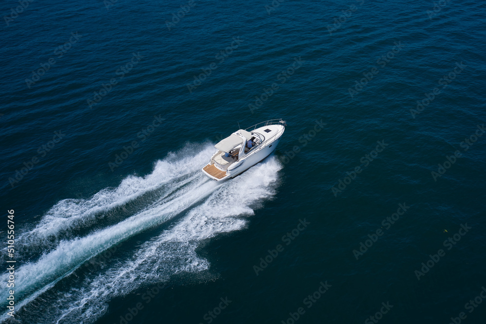 White yacht fast moving on clear water aerial side view. A large white boat at high speed on the water leaves a white trail, top view.