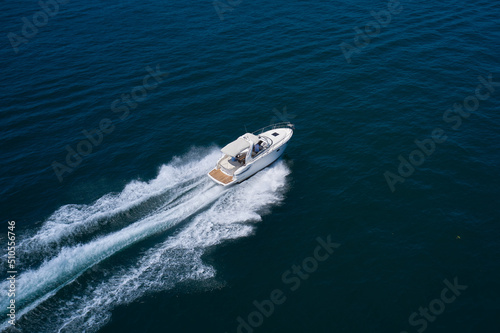White yacht fast moving on clear water aerial side view. A large white boat at high speed on the water leaves a white trail, top view. © Berg