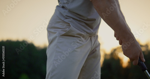 Golfer hand swinging club putter on sunset golf course. Man hitting ball outside