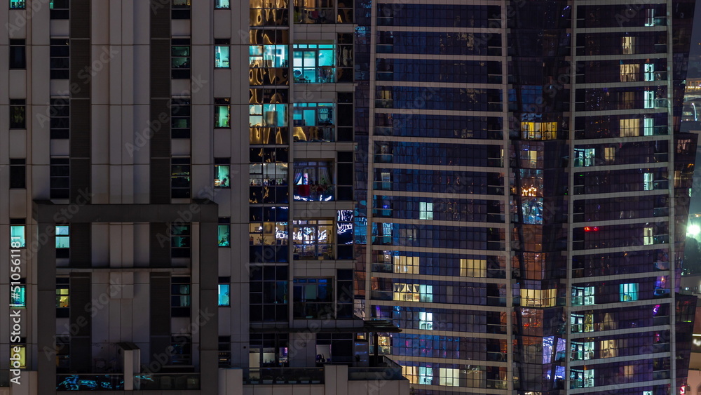 Apartment windows of a glazed skyscraper glow at night with city lights reflection aerial timelapse.