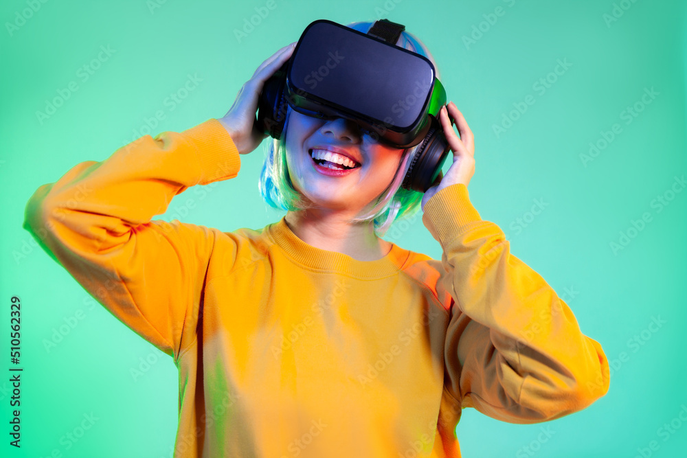 Metaverse concept, happy young asian woman in yellow sweatshirt wearing vr headset playing and watching on the green screen background. Metaverse concept, happy young asian woman in yellow sweatshirt wearing vr headset playing and watching on the green screen background.