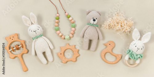 Infant toys on a pastel beige background. Wooden and crocketed baby handmade toys for a banner in eco style. Baby toys concept. Wooden rattles, knitted teddy bear and teething beads top view.