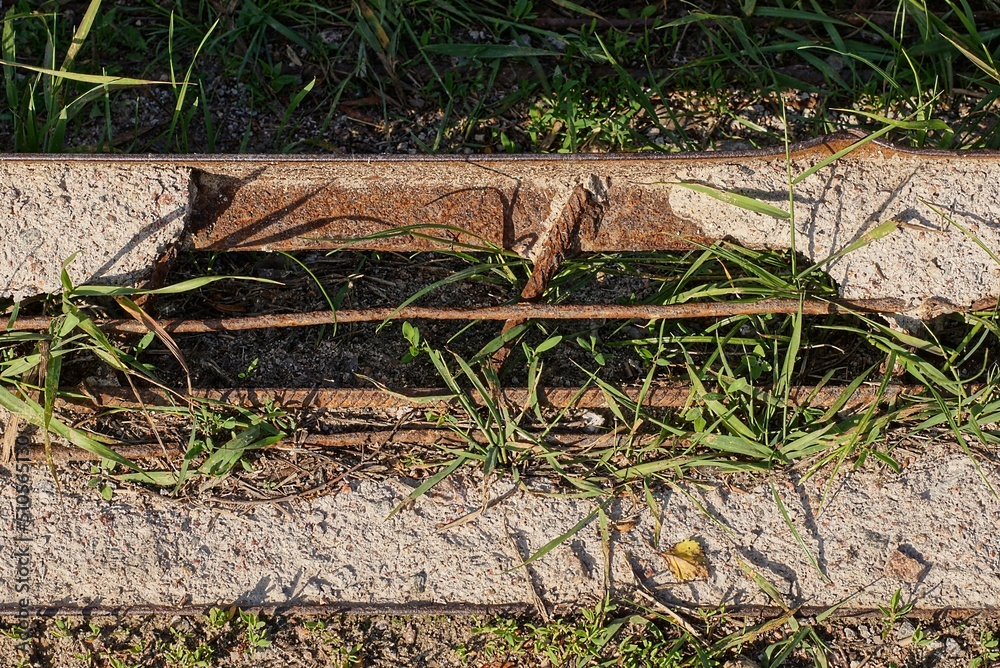 a piece of an old broken concrete pillar with rusty brown iron bars lies in the green grass on the street a piece of an old broken concrete pillar with rusty brown iron bars lies in the green grass on the street