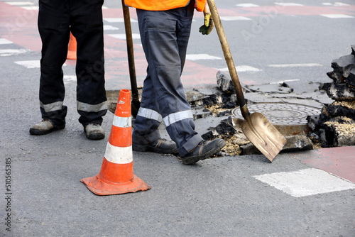 Workers repair the road surface, man with shovel near the sewer manhole. Construction and repairing works in city