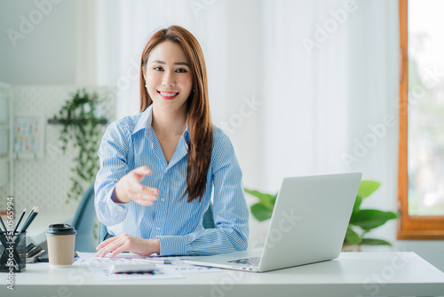 Asian businesswoman extending her hand to camera in greeting gesture and shaking hands at financial accounting business concept desk