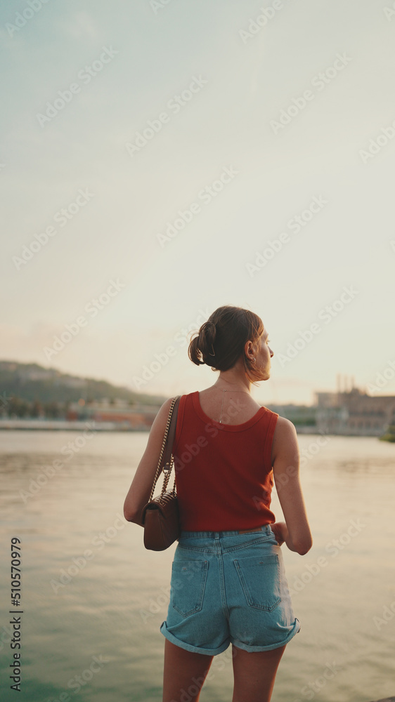 Girl stands on the embankment and looks at the bay. Young woman looks at the sea in the morning time. Back view Girl stands on the embankment and looks at the bay. Young woman looks at the sea in the morning time. Back view