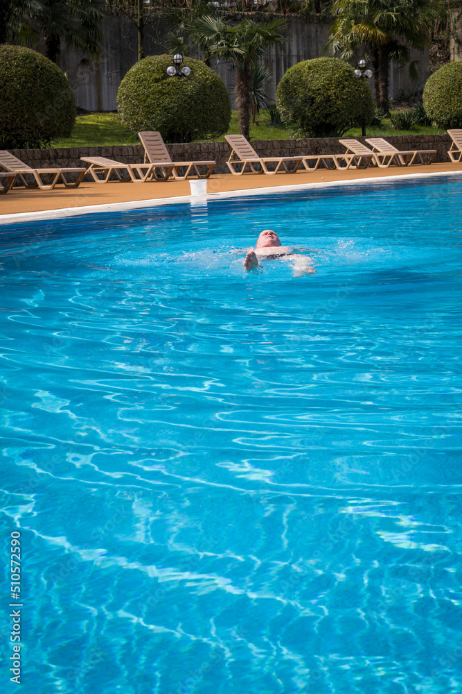 An elderly gray-haired retired man swims in the pool. The concept of a healthy active lifestyle in old age