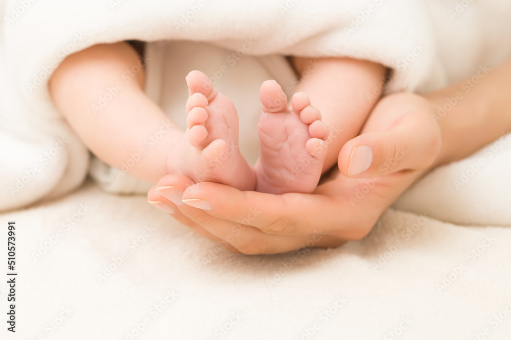 Young adult mother hand holding and showing newborn cute small bare feet on white soft blanket in bed. Lovely emotional, sentimental moment. Closeup. Parent love. Front view. Young adult mother hand holding and showing newborn cute small bare feet on white soft blanket in bed. Lovely emotional, sentimental moment. Closeup. Parent love. Front view.