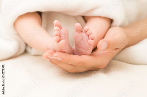 Young adult mother hand holding and showing newborn cute small bare feet on white soft blanket in bed. Lovely emotional, sentimental moment. Closeup. Parent love. Front view.