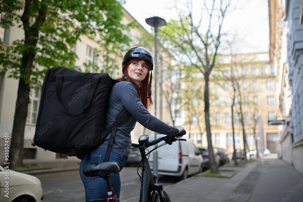 Female courier on bicycle with thermal backpack on way to deliver food to customers.